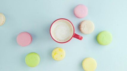 Top view of multicolored French Macarons cookies and a cup of coffee on a pastel blue background