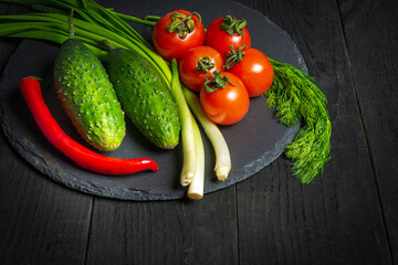 Big set for fresh vegetable salad. Red tomatoes and green young onions with cucumber on a vintage brown plate