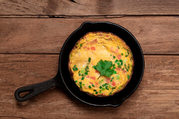 Egg breakfast food omelet has vegetable in pan on wood table.