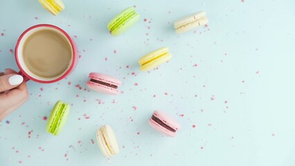 Top view of colorful cookies, French Macarons, and a cup of coffee on a pastel blue background with beautifully scattered confetti