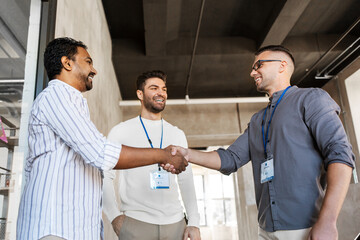 Obraz premium business, gesture and partnership concept - happy businessmen name tags making handshake at office