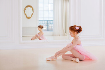 Little ballerina girl in a pink tutu and pointe shoes posing in white studio