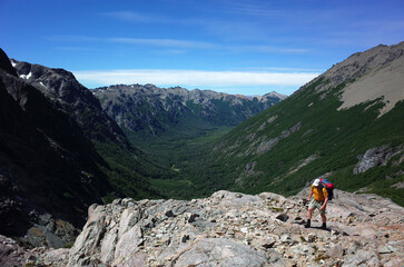 Fototapeta premium Trekking in Patagonia, Argentina hiking trail, Man with backpack walking on rocky plateau with view of green valley in Nahuel Huapi National Park, Mountain landscape nature of Patagonia