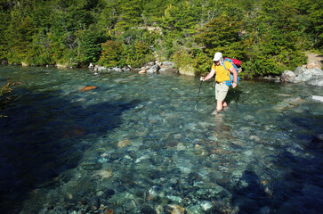 Summer hike hiker man with backpack crossing river cristal clear water, Trekking in Argentina Nahuel Huapi National Park, Patagonia adventure