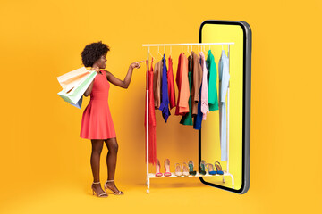 Black Lady Shopping Choosing Clothes In Huge Phone, Yellow Background
