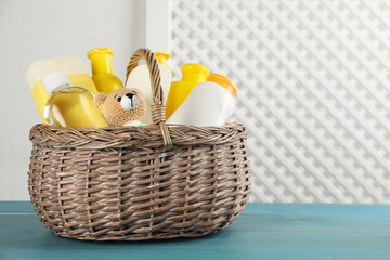 Wicker basket full of different baby cosmetic products and toy on light blue wooden table. Space...