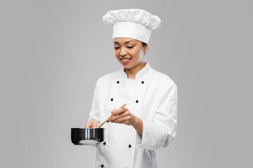 culinary and people concept - happy smiling female chef in toque and jacket with saucepan cooking food over grey background