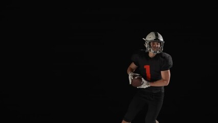 American football player running, catches pass, dodges an rival attack against black background. Players run attacking to score touchdown points. Professional athletes fight for the ball. Slow motion.