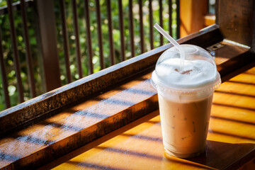 ice cappuccino in plastic cup on wooden table. Shadow and contrast  with copy space in warm color...