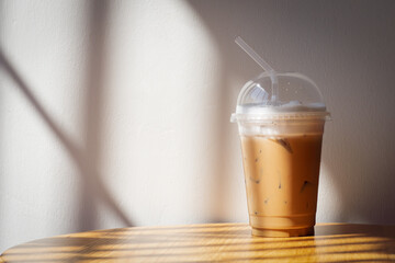 Ice cappuccino in plastic cup on wooden table. Shadow and warm light with copy space in warm color tone.