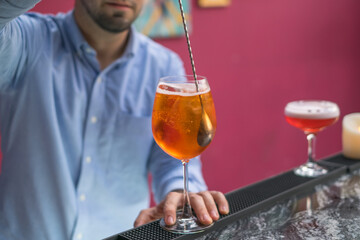 The bartender makes Aperol spritz summer cocktail in mister glass. Close up photo, process, bar. High quality photo