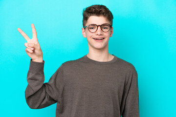 Teenager Russian man isolated on blue background smiling and showing victory sign