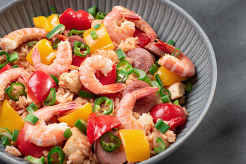 Jambalaya rice with chicken, shrimp, sausage and vegetables in plate on gray concrete table