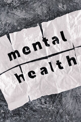 Mental health text on crumpled and torn piece of paper which has been reassembled with sticky tape, psychology and emotional healing