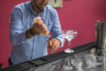 Bartender makes cocktail in mister glass. Close up photo, process, bar, Pink wall, restaurant. High quality photo. 