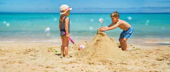 Sibling boy building a sandcastle at the beach in summer