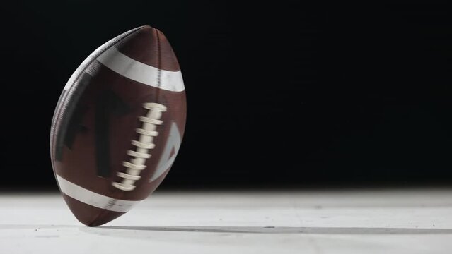 American football rotates against black background close up. An oval american football ball spins in slow motion in a backlit dark stadium. Extreme sport spirit concept. Masculine aggressive game.