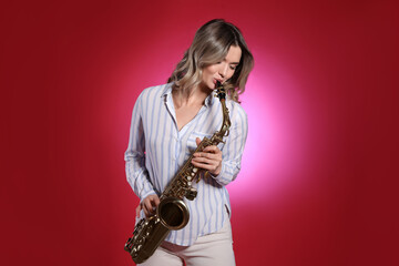 Fototapeta premium Beautiful young woman playing saxophone on red background