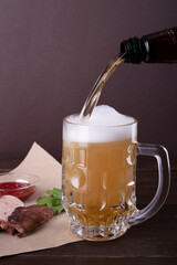 a glass of beer with foam on a wooden table against the background of pieces of fried meat