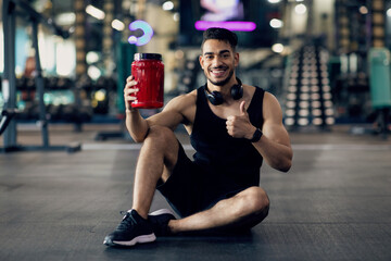 Fototapeta na wymiar Handsome Muscular Middle Eastern Guy Advertising Fitness Supplements While Posing At Gym