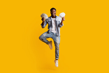 Lucky african american guy holding bunch of money and jumping