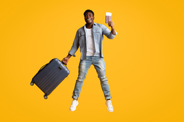Emotional african american guy with suitcase and flight tickets jumping