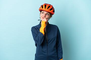 Young cyclist woman isolated on blue background and looking up - obrazy, fototapety, plakaty