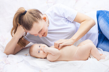 young happy mother together with her newborn baby lie cheerfully on a white bed