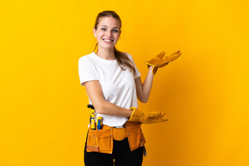 Young electrician woman isolated on yellow background extending hands to the side for inviting to...