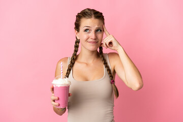 Young woman with strawberry milkshake isolated on pink background having doubts and thinking