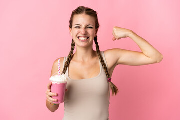 Young woman with strawberry milkshake isolated on pink background doing strong gesture