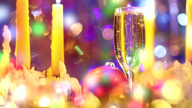 Close up of burning candles and glass of champagne with funny bubbles against Christmas tree background twinking garland lights seamless looping footage selective focus.