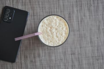High angle view of Lassi in glass and mobile phone over gray background with copy space 