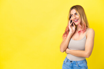 Young woman over isolated yellow background keeping a conversation with the mobile phone