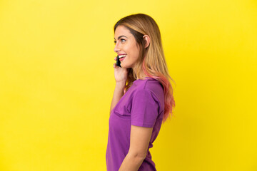 Young woman using mobile phone over isolated yellow background laughing in lateral position