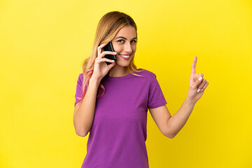 Young woman using mobile phone over isolated yellow background showing and lifting a finger in sign of the best