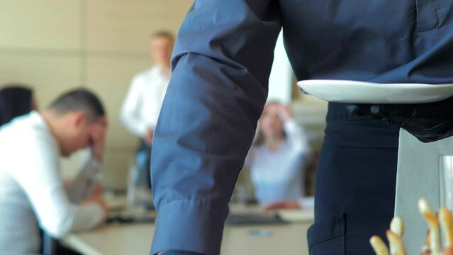 The waiter lays out food for catering.Beautifully decorated banquet table with canapes snacks in the office.Meals for a group of people on the buffet system indoors.The waiter of the catering business