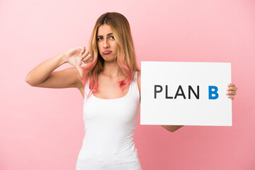 Young woman over isolated pink background holding a placard with the message PLAN B and doing bad...