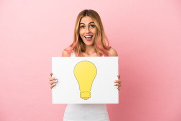 Young woman over isolated pink background holding a placard with bulb icon with happy expression