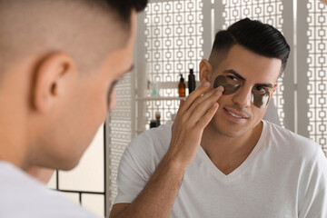 Fototapeta premium Man applying dark under eye patch near mirror at home