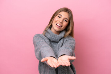 Young caucasian woman isolated on pink bakcground holding copyspace imaginary on the palm to insert an ad