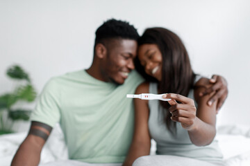 Smiling millennial african american male and female rejoice and show positive pregnancy test in bedroom