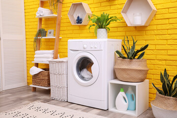 Laundry room interior with modern washing machine near yellow brick wall