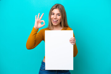 Fototapeta premium Young caucasian woman isolated on blue background holding an empty placard and doing OK sign