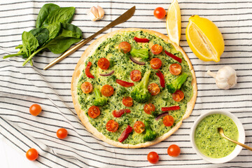 vegan pizza with broccoli and spinach pesto sauce, tomatoes on a white table