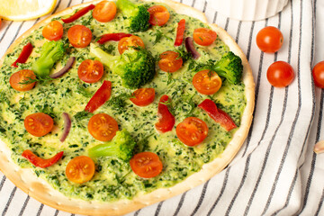 vegan pizza with broccoli and spinach pesto sauce, tomatoes on a white table