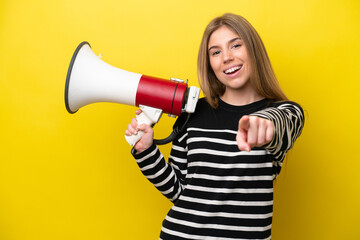 Young caucasian woman isolated on yellow background holding a megaphone and smiling while pointing to the front