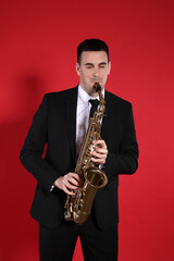 Naklejka premium Young man in elegant suit playing saxophone on red background