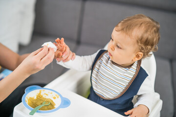 Cute baby boy got dirty while eating and mother is cleaning him.