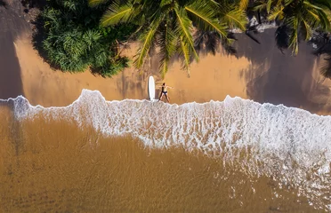 Foto op Aluminium Aerial photo of surfer lying next to surfboard on the sandy ocean shore in STAR pose and sun tanning under tall palm trees. Soft waves washing his legs on Sri Lank beach island Exotic vacation concept © Soloviova Liudmyla